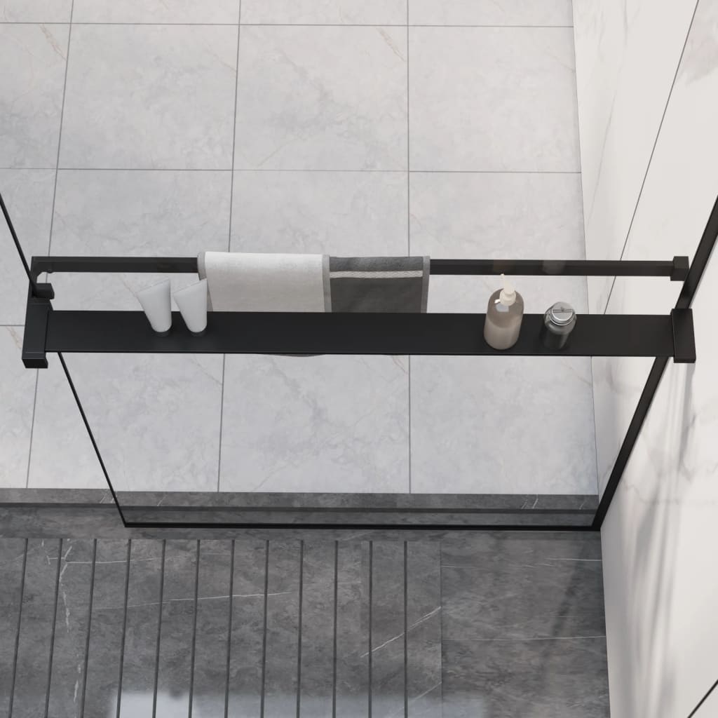 Black aluminum shower shelf mounted on glass wall, holding towels, bottles, and soap.