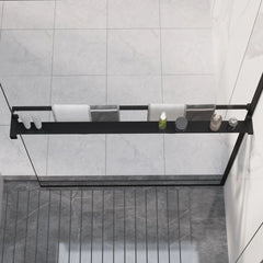 Black aluminum shower shelf mounted on walk-in shower wall with glass panels, holding shampoo bottles.
