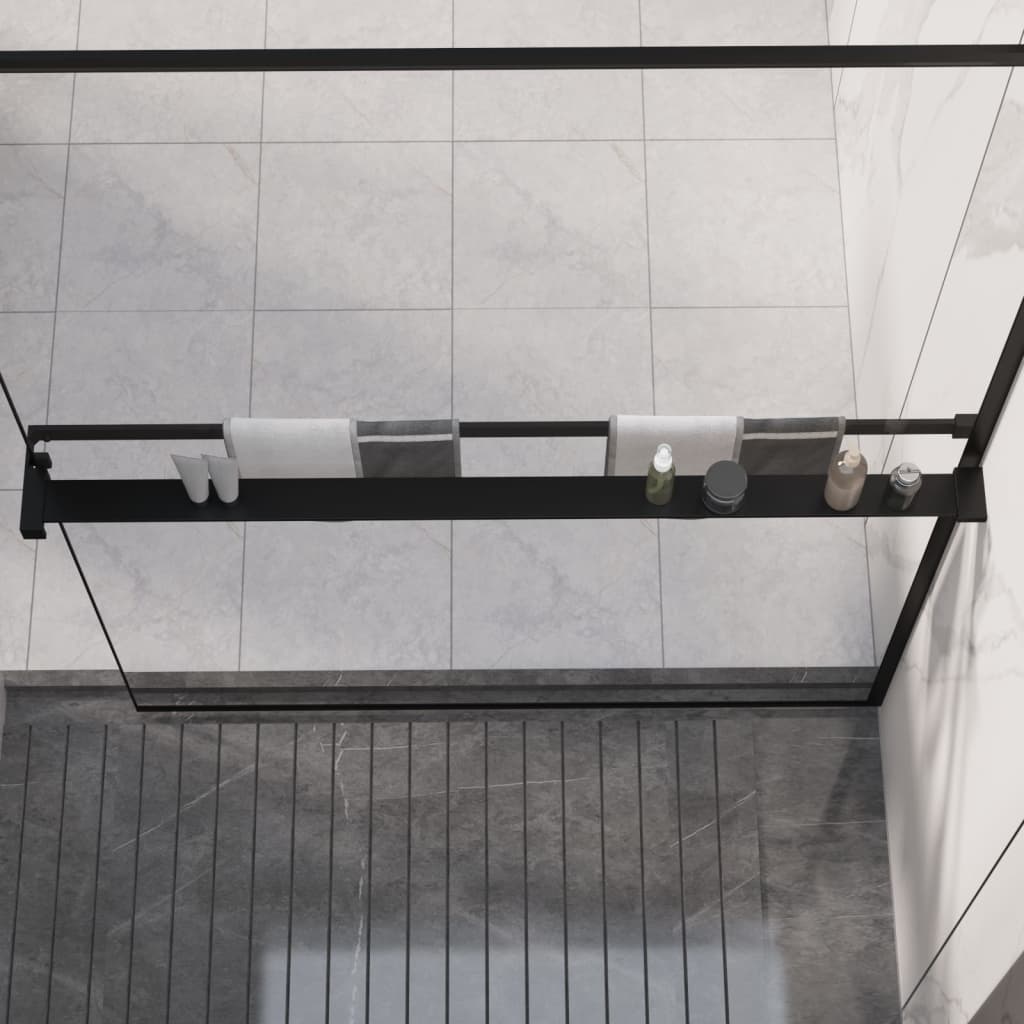 Black aluminum shower shelf mounted on glass panel, holding towels, shoes, and bottles.