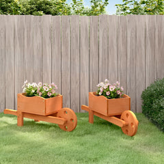Two wooden wheelbarrow planters with pink flowers, placed on grass against a fence.