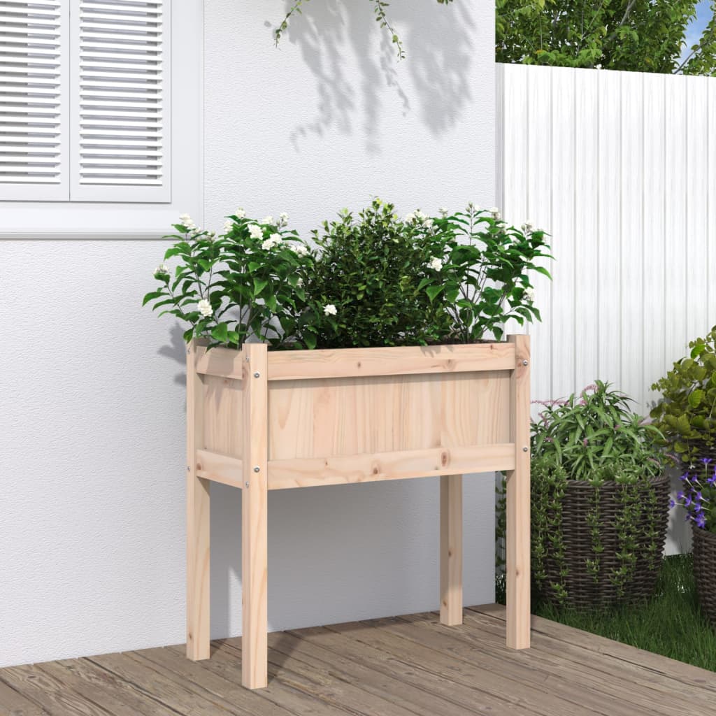 Wooden elevated garden planter with legs filled with green plants against a white wall.