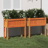 Two brown solid pine wood garden planters with legs filled with green plants on grass.