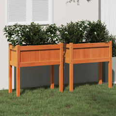 Two brown solid pine wood garden planters with legs filled with green plants on grass.