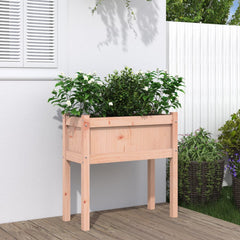 Wooden raised garden planter with legs, planted with green shrubs, on a patio.