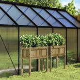 Two elevated wooden garden planters with legs, holding white flowering plants, in a greenhouse setting.