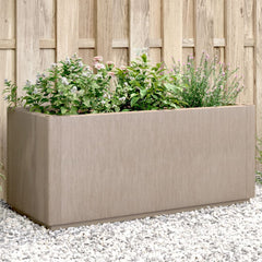 A light brown rectangular planter filled with various green plants and flowers, set on white gravel.
