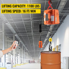 Orange 1100 lbs electric hoist winch with remote control lifting a yellow drum in a warehouse.