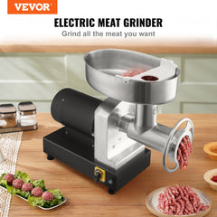 Silver Bostome heavy-duty electric meat grinder on a kitchen counter, grinding meat into a bowl with sausage and veggie plates nearby.