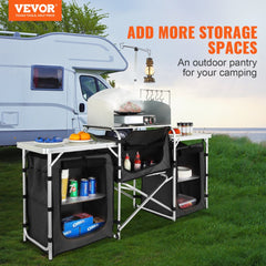 Folding aluminum camping kitchen table in black with storage shelves and bag, set up outdoors near an RV.