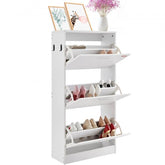 White shoe cabinet with three flip drawers, storing various shoes, beside flowers.