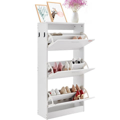 White shoe cabinet with three flip drawers, storing assorted shoes and flanked by flowers and frames.