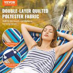 Two-person striped hammock with steel stand set up outdoors in a sunny backyard.