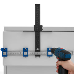 Aluminum alloy cabinet hardware jig with center punch, rulers, and clamps on a drawer.