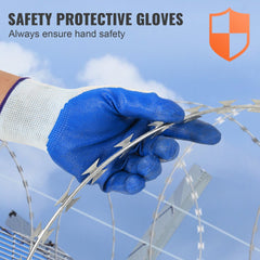 Hand wearing blue safety gloves handling galvanized razor barbed wire coils.