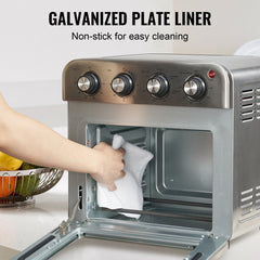 Hand wiping the interior of an open stainless steel air fryer toaster oven with a cloth.