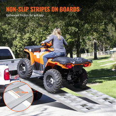 Two 72-inch by 15-inch aluminum loading ramps with non-slip stripes on a truck tailgate next to an orange ATV.