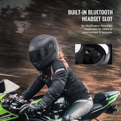 Black motocross helmet with built-in Bluetooth slot, worn by rider on green motorcycle.