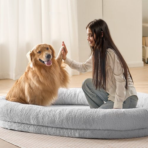 A woman high-fives a golden retriever on a large gray faux rabbit fur dog bed.
