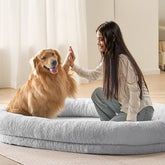 A woman high-fives a golden retriever on a large gray faux rabbit fur dog bed.