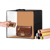 A portable photo studio light box with a brown handbag inside and multiple backdrops.