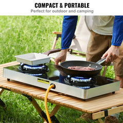 A man uses a portable 28-inch 2-burner gas cooktop with tempered glass on a folding table outdoors while camping.