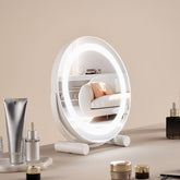 A white 12-inch round LED vanity mirror with smart touch controls, 3-color lighting, and a 5X magnifying insert on a stable base.