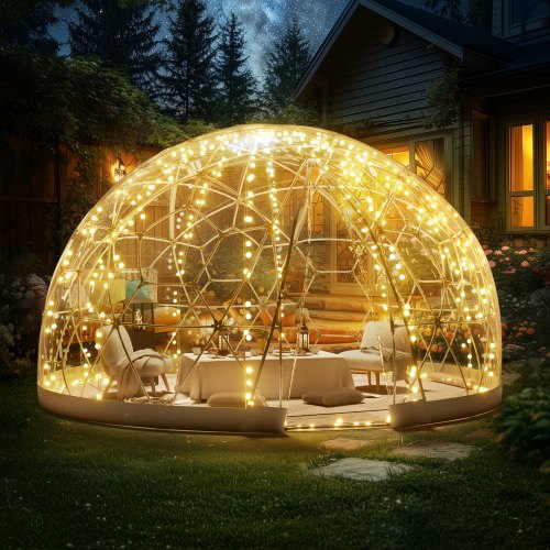 A 9.5-foot transparent PVC dome bubble tent in a garden, lit with string lights and set up with chairs and a table.