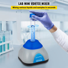 A hand in blue glove holds a 50ml tube on a compact blue and gray mini vortex mixer in a lab setting.
