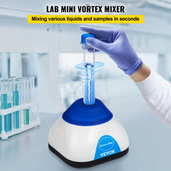 Compact blue and white mini vortex mixer shaking a blue-capped test tube held by a gloved hand in a lab setting.