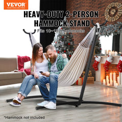 A steel hammock stand supporting a beige hammock with a couple sitting in it, fitting 10-13 ft hammocks up to 450 lbs.