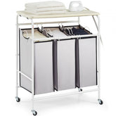 White rolling laundry sorter cart with three fabric bins, ironing board top, and lockable wheels.