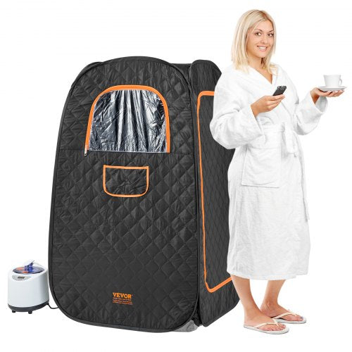 A blonde woman in a white robe stands beside a black Bostome 1200W personal steam sauna tent with orange accents and a small steamer unit.