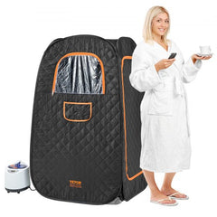 A blonde woman in a white robe stands beside a black Bostome 1200W personal steam sauna tent with orange accents and a small steamer unit.