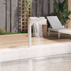 Silver stainless steel arc pool fountain cascading water into a pool beside a wooden deck and lounge chair.