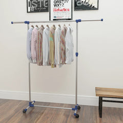 Silver adjustable stainless steel clothes rack with clothes hanging, on wheels and wood floor.