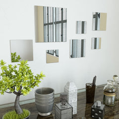 Seven square frameless glass mirrors in varying sizes arranged on a white wall.
