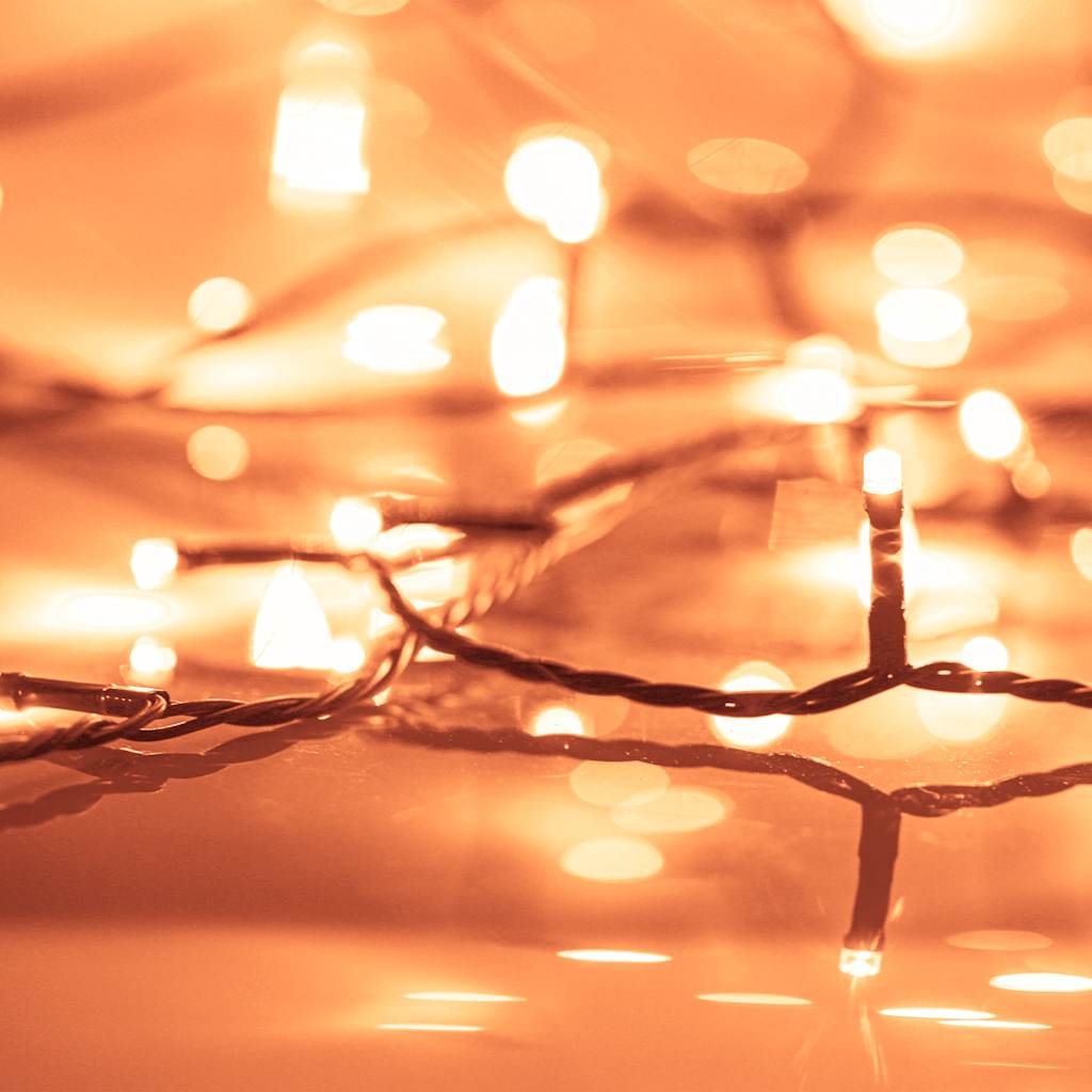 Warm white LED string lights with glowing bulbs on a flexible wire against an orange background.