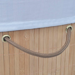 Oval natural bamboo laundry hamper with brown rope handles and white liner.