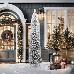 A 7ft slim flocked snow artificial Christmas tree with green PVC branches on a stand, displayed outdoors near a front door with holiday decorations.