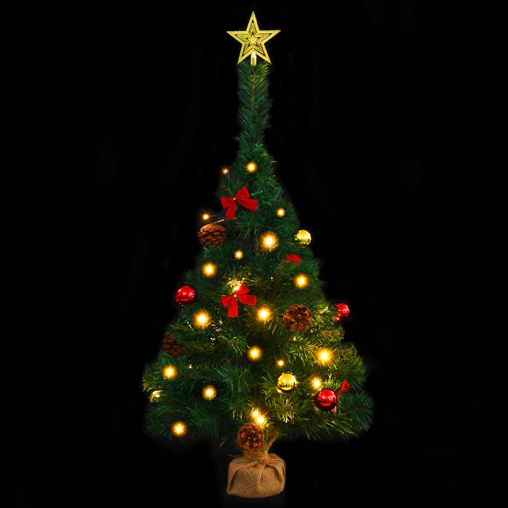 A 2ft pre-lit artificial Christmas tree in green with gold star topper, red baubles, pine cones, bows, and warm LED lights on a linen-wrapped base.