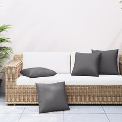 Four anthracite polyester throw pillows on a white wicker outdoor sofa.