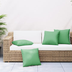 Four green polyester throw pillows, 23.6x23.6 inches, on a white wicker outdoor sofa.