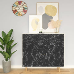 A modern room with a black marble-effect cabinet, colorful wall clock, abstract art, potted plant, and vase.