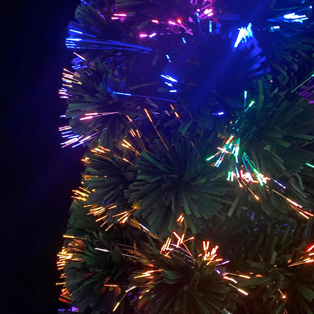 A 5 ft slim artificial fiber optic Christmas tree with black-green PVC needles and multicolored glowing tips.