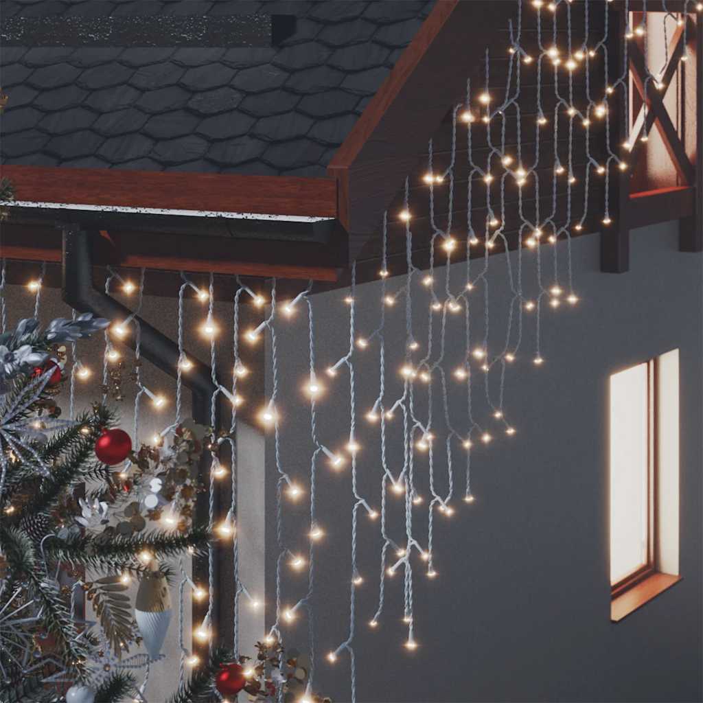 Warm white LED curtain icicle lights hang from a roof and gutter, next to a decorated tree.