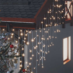 Warm white LED curtain icicle lights hang from a roof and gutter, next to a decorated tree.
