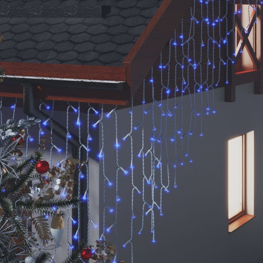 Blue LED curtain icicle lights draped over a house facade with a Christmas tree nearby.