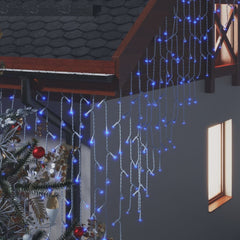 Blue LED curtain icicle lights draped over a house facade with a Christmas tree nearby.