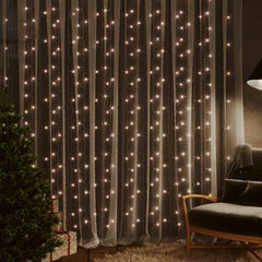 LED curtain fairy lights with 300 warm white LEDs draped over a window in a cozy room with a Christmas tree and chair.