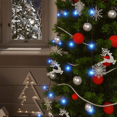 A decorated Christmas tree with blue fairy lights and ornaments by a snowy window.